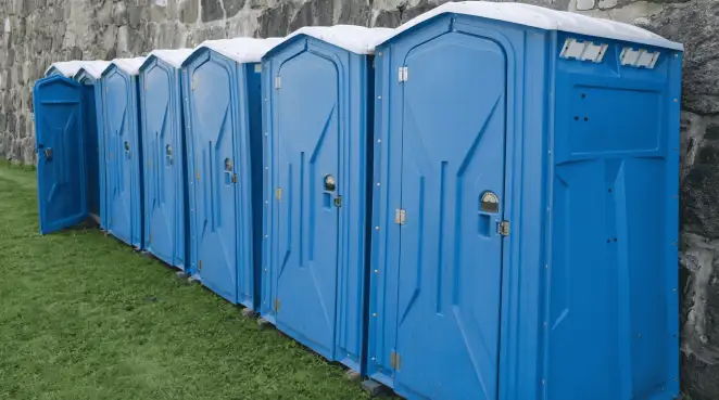 Row of blue portable toilets lined up on grass against a stone wall for event sanitation in Louisville, KY