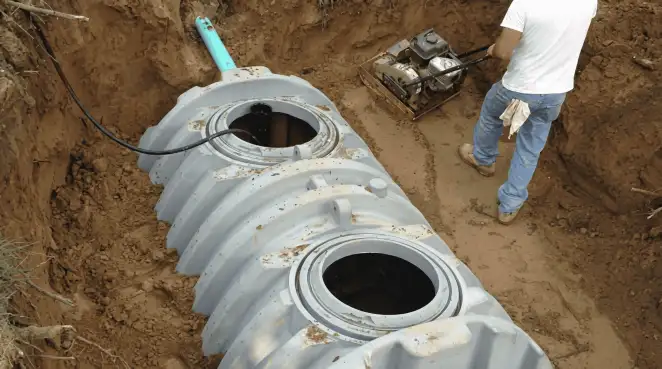 Septic tank installation showing a technician compacting soil around a new poly septic tank in an excavation pit in Louisville, KY